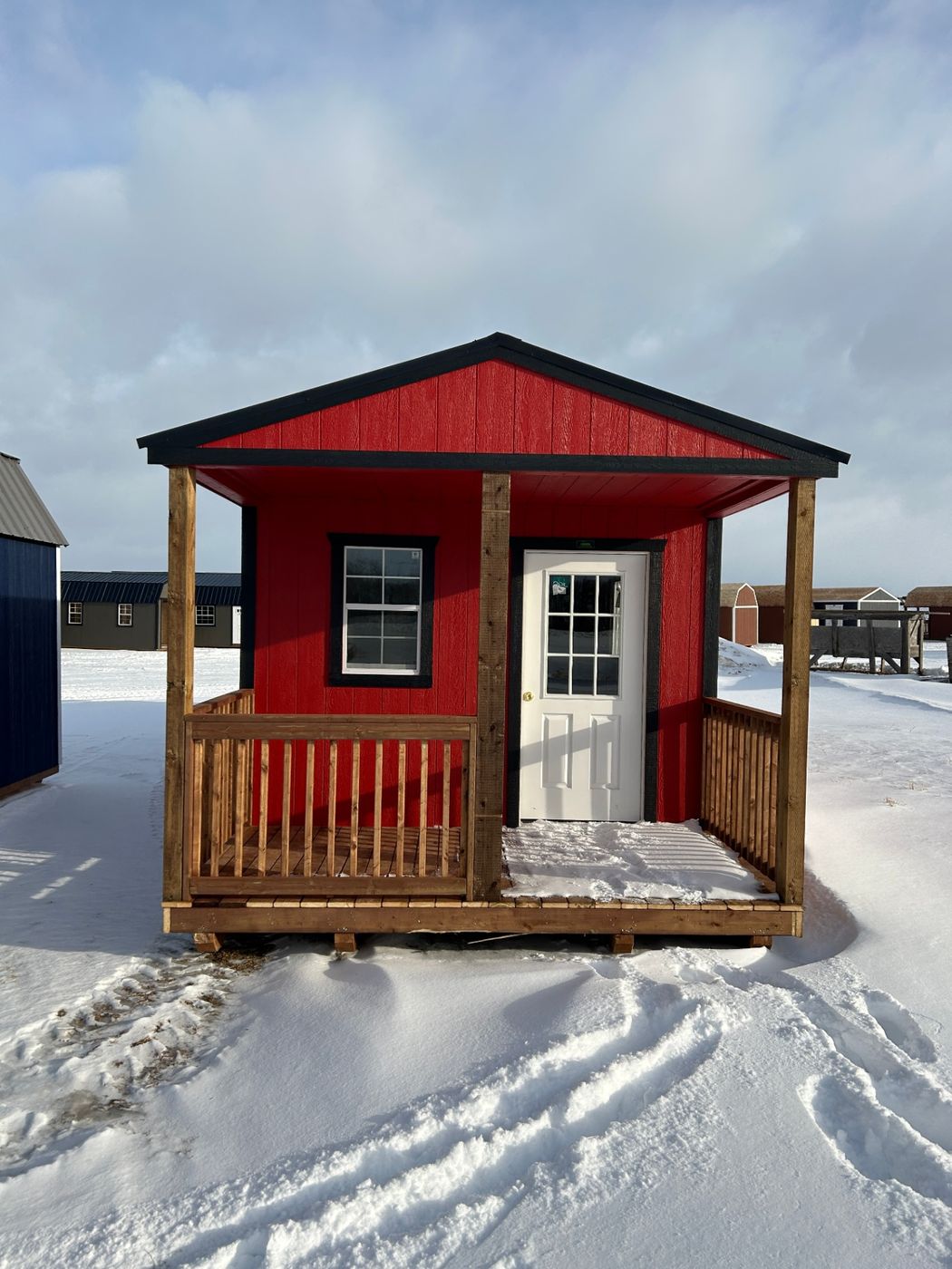 Premier red gabled cabin with black metal roof and covered porch, front view in winter Alberta