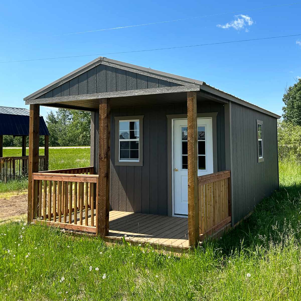 Premier grey gabled cabin with covered porch and cedar posts, set on grassy lot in rural Alberta